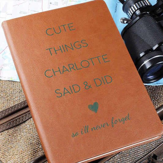 Brown notebook with text 'Cute things Charlotte said & did so I'll never forget' on a textured surface with a camera.