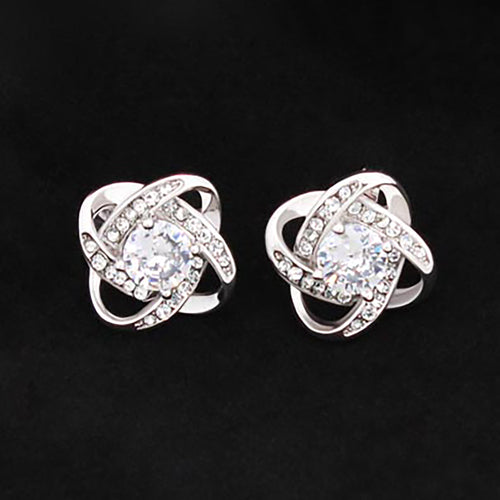 Pair of 14k white gold plated Love Knot stud earrings featuring sparkling cubic zirconia center stones on a dark background