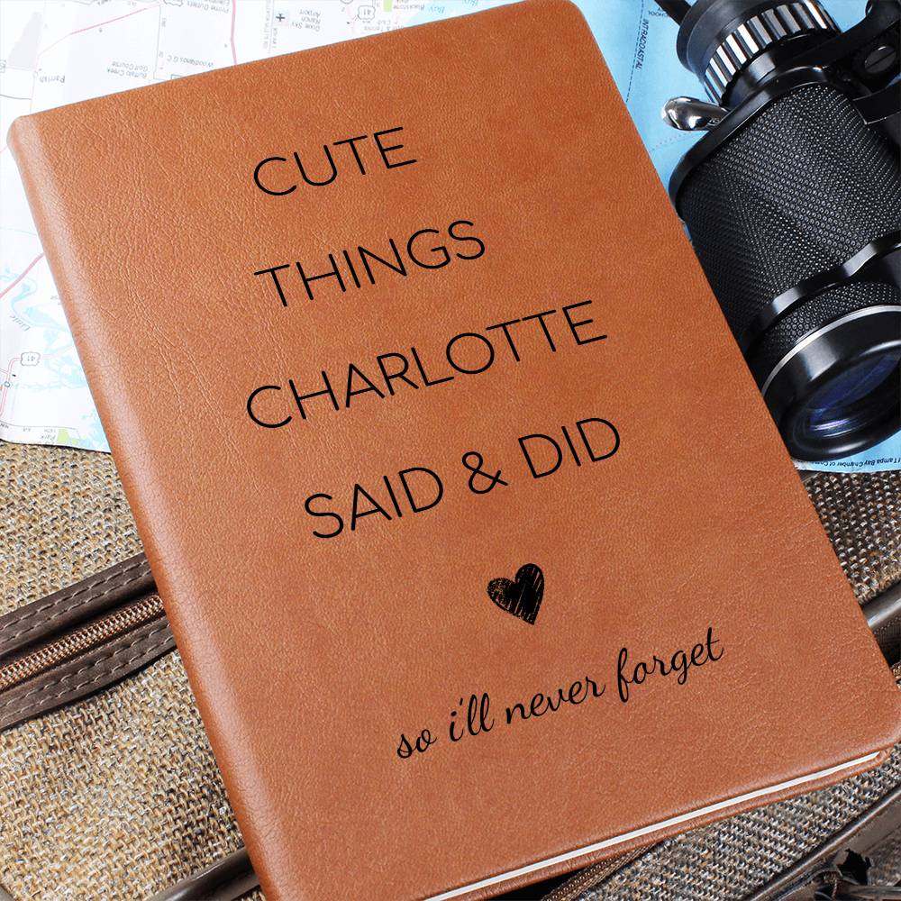 Brown notebook with text 'Cute things Charlotte said & did so I'll never forget' on a textured surface with a camera.