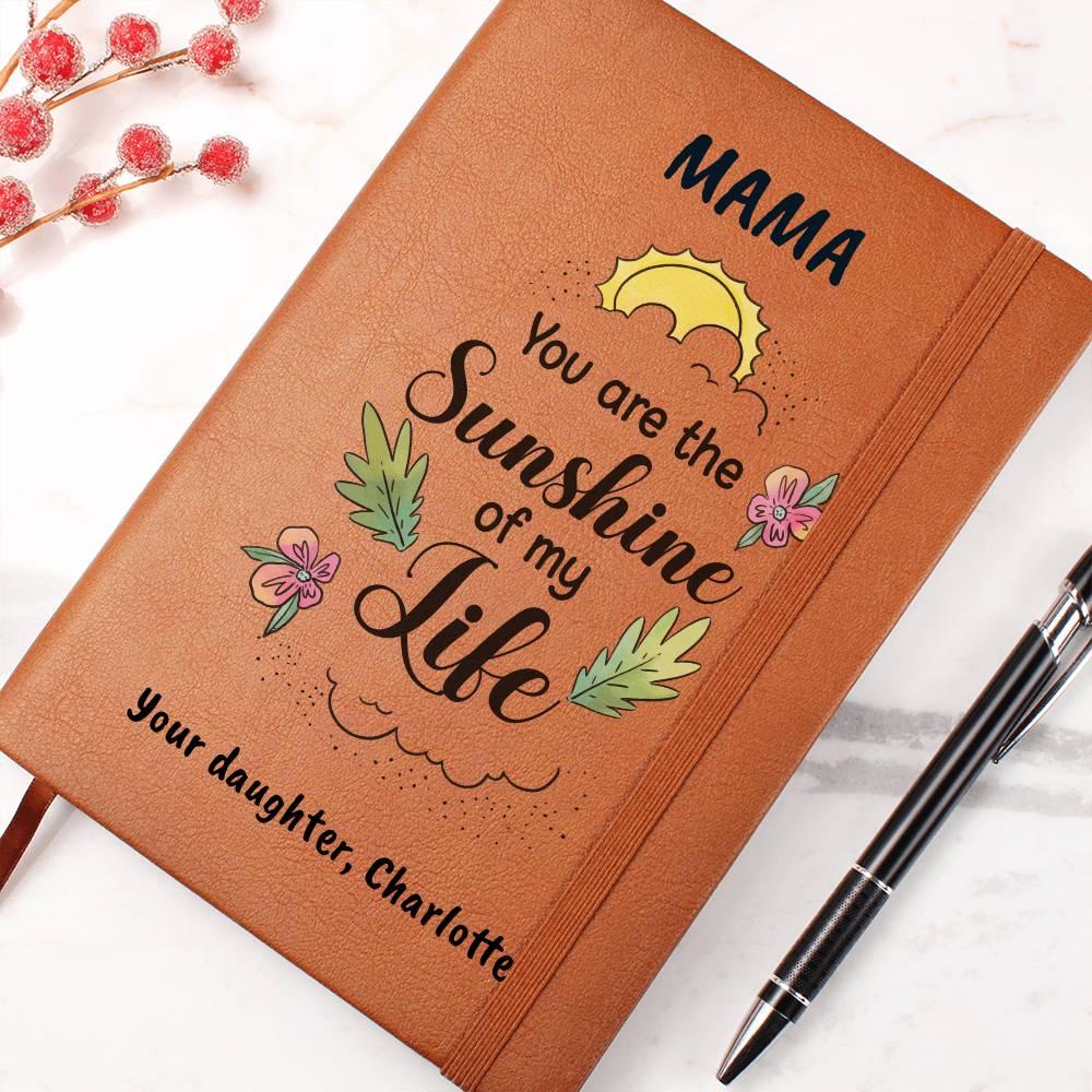 Brown notebook with 'Mama, you are the sunshine of my life' text and a pen on a white background