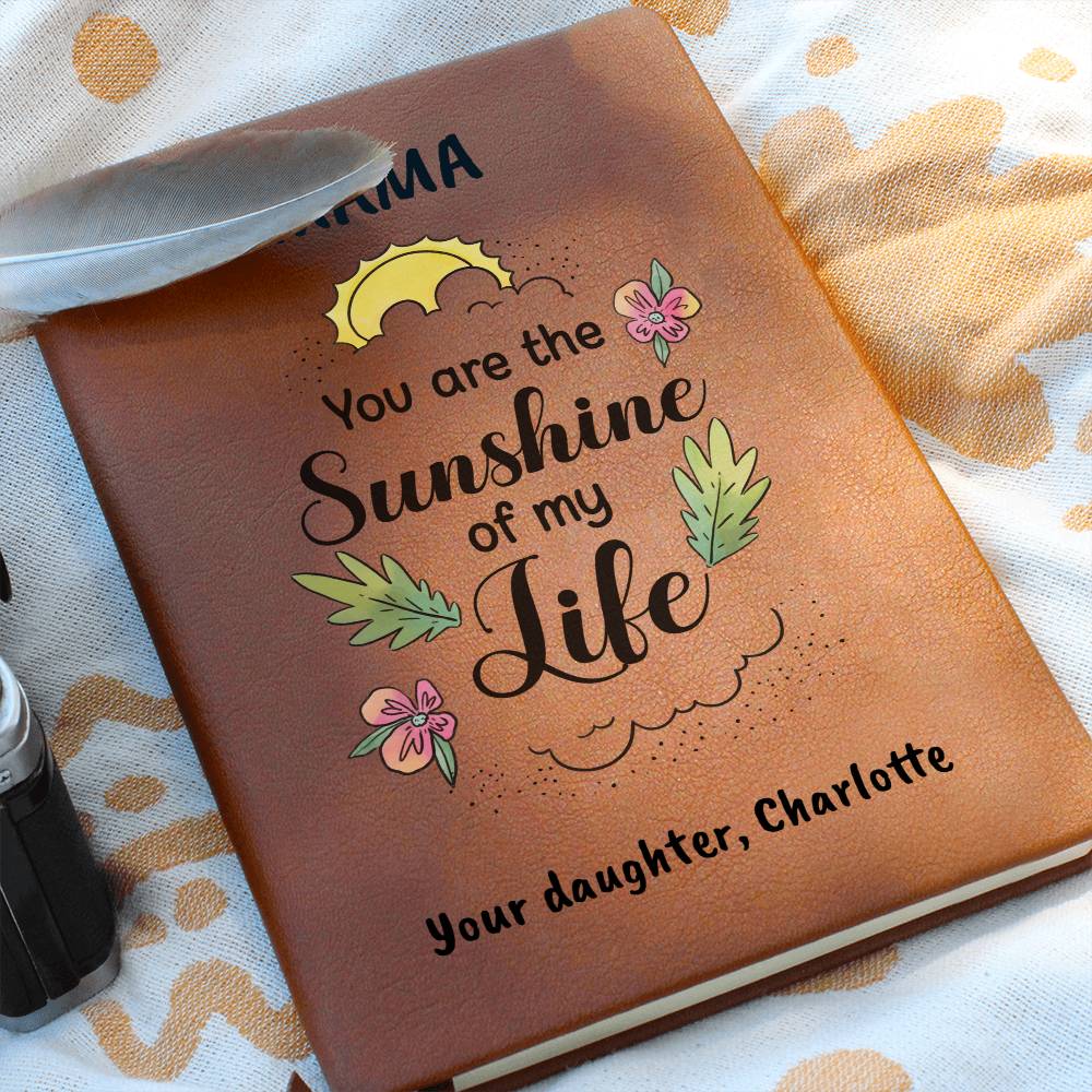 Brown leather notebook with 'You are the Sunshine of my Life' text and floral designs on a patterned fabric background.