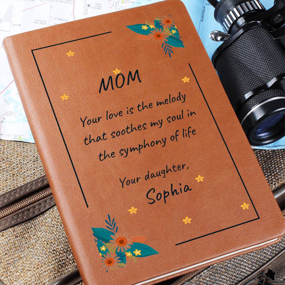 Brown leather notebook with floral designs and a heartfelt message to 'Mom' on a textured surface.