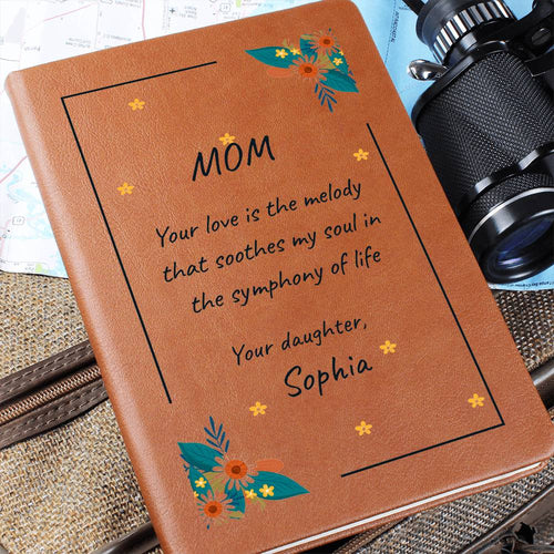 Brown leather notebook with floral designs and a heartfelt message to 'Mom' on a textured surface.
